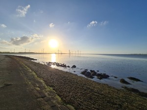 Zonsondergang bij de kust met windturbines aan de horizon.