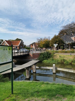 Dorpsbrug over kanaal met fietsroutebord en houten steiger